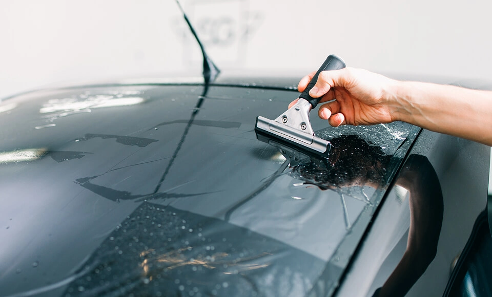 IMAGEM ILUSTRATIVA - HOMEM APLICANDO PELÍCULA EM TETO DE CARRO COM ESPÁTULA