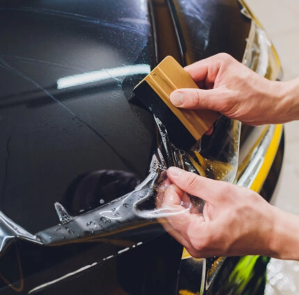 IMAGEM ILUSTRATIVA - HOMEM APLICANDO PELÍCULA AUTOMOTIVA EM CAPÔ COM ESPÁTULA