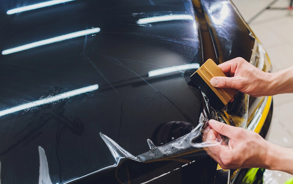 IMAGEM ILUSTRATIVA - HOMEM APLICANDO PELÍCULA AUTOMOTIVA EM CAPÔ COM ESPÁTULA